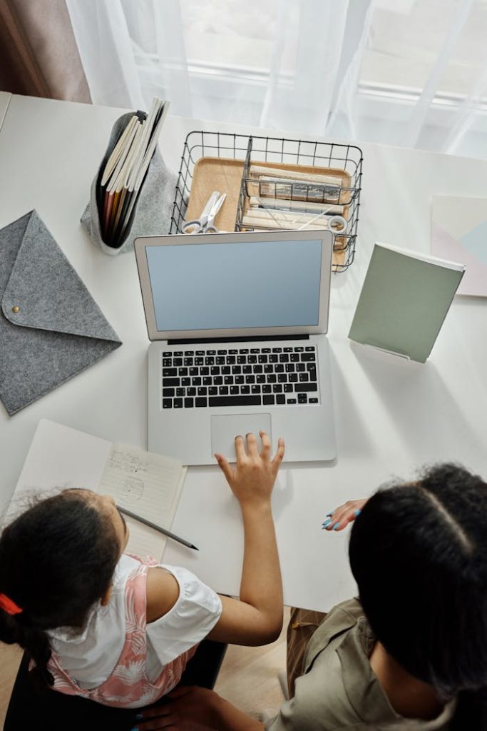 Overhead view of a mother helping her daughter with online learning at home.