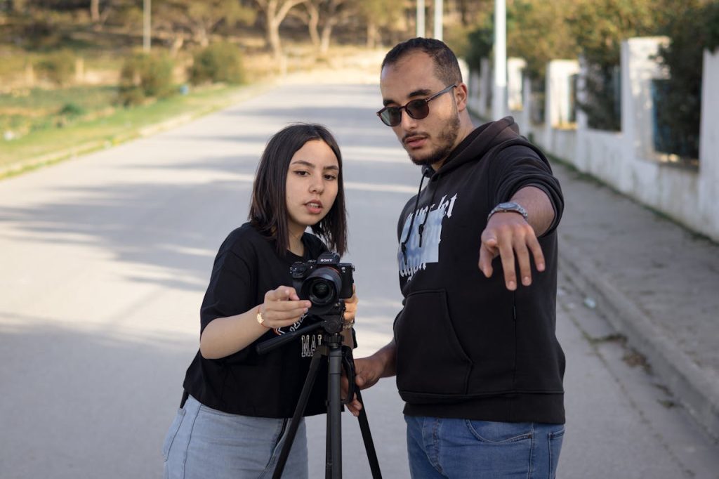 Two young adults collaborating on a film project outdoors with a camera on a tripod.